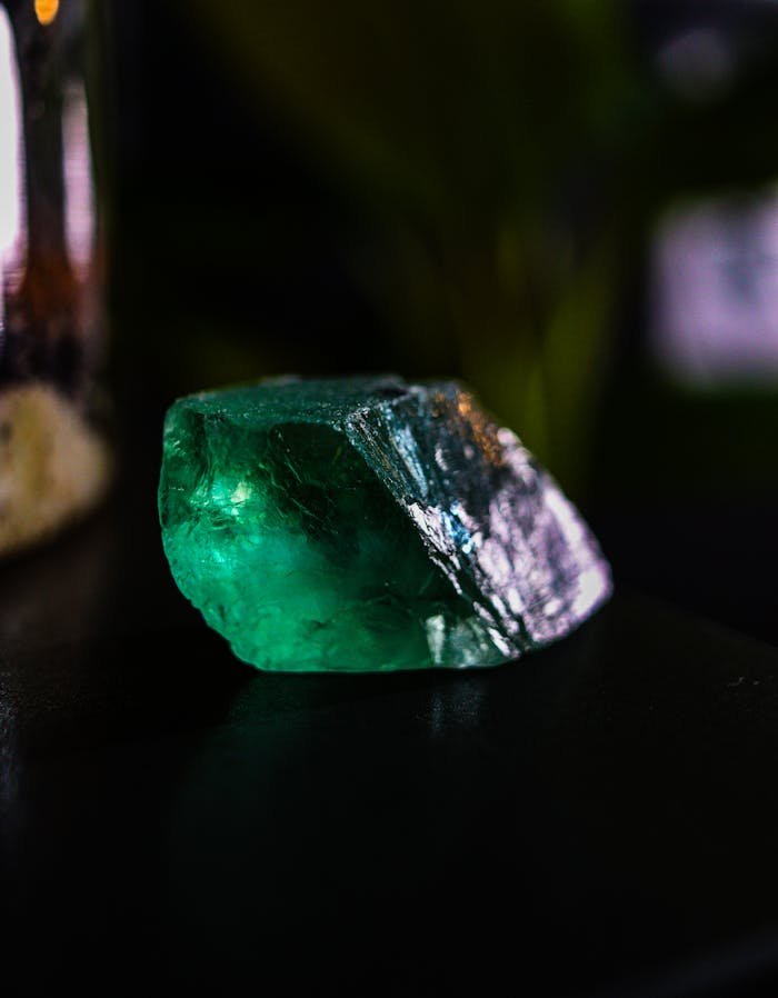 Close-up of a raw green emerald gemstone placed on a dark surface, captured in rich lighting.